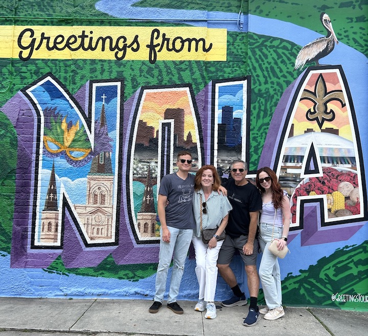 A group of people posing for a photo in front of a mural

Description automatically generated