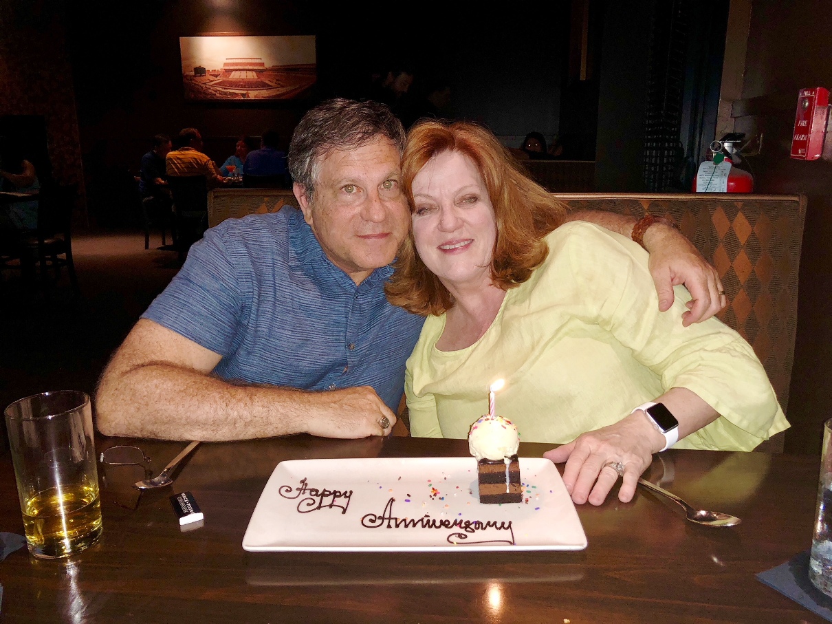 A person and person sitting at a table with a cake

Description automatically generated