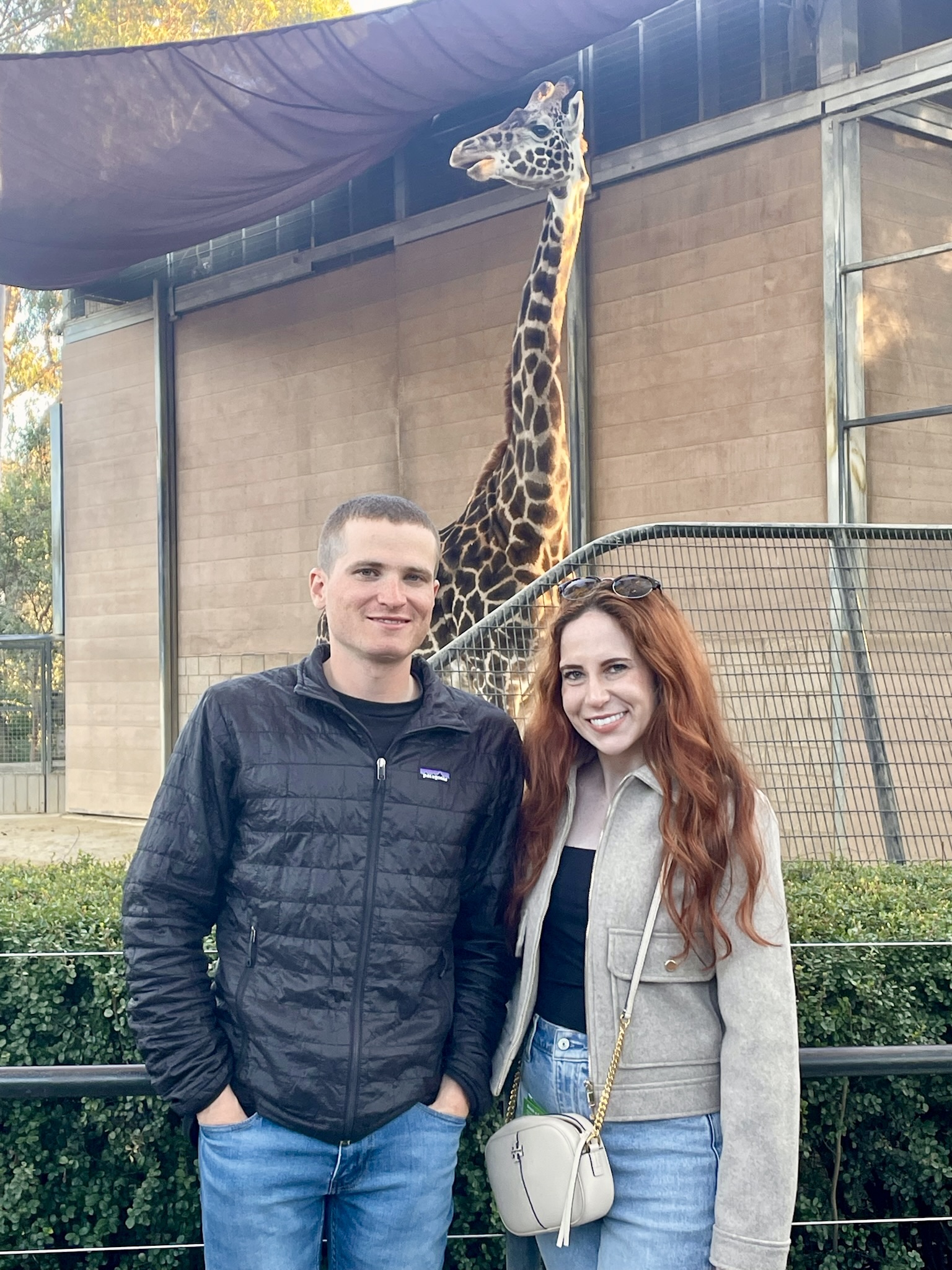 A person and person standing in front of a giraffe
Description automatically generated