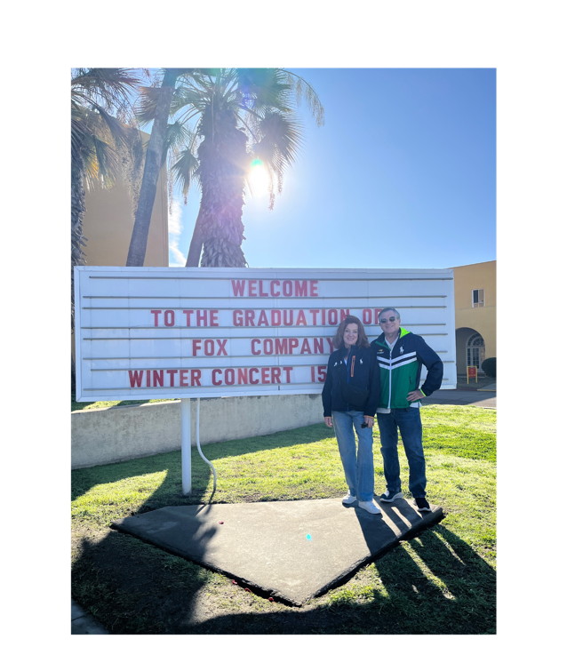 A person and person standing next to a sign
Description automatically generated